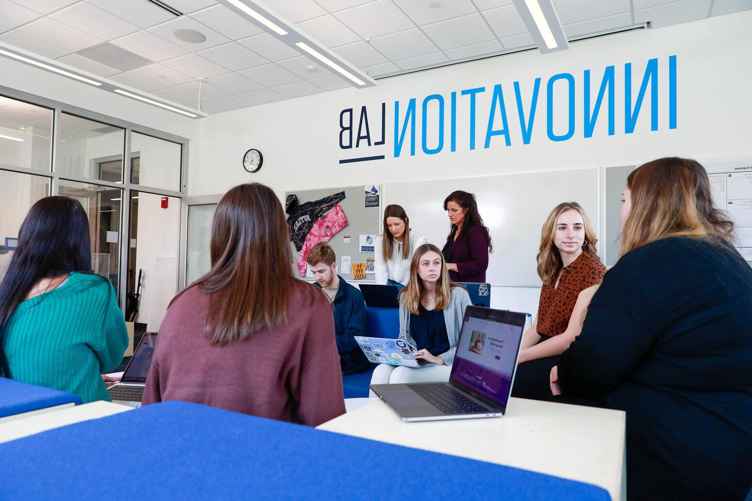 男女学生坐在蓝色和白色的座位上. 创新实验室印在白墙上